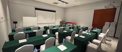 Un salón de conferencias con varias mesas, sillas y una pantalla de proyector.