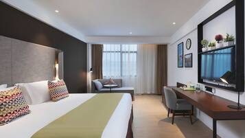 A hotel room with a bed, a desk, a chair, a television, and a window with curtains.