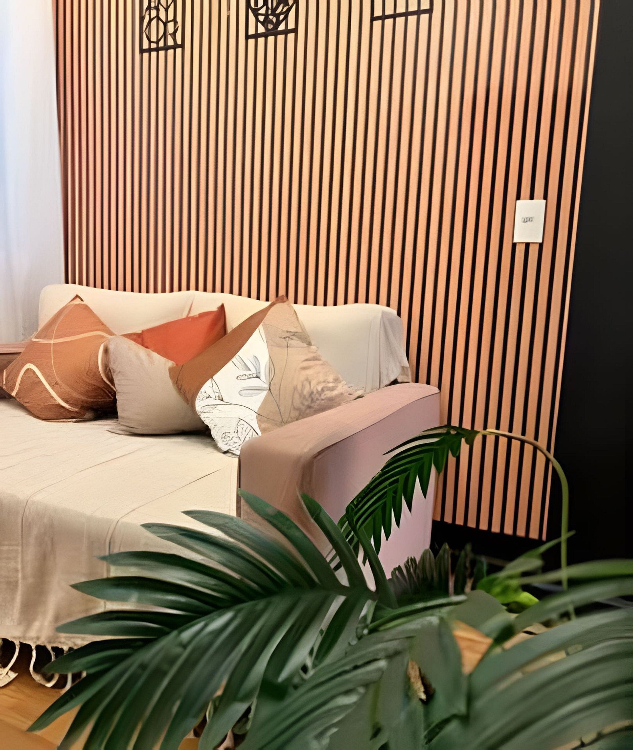 Quarto com sofá, almofadas, uma planta e parede com linhas verticais.