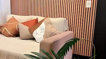 Quarto com sofá, almofadas, uma planta e parede com linhas verticais.