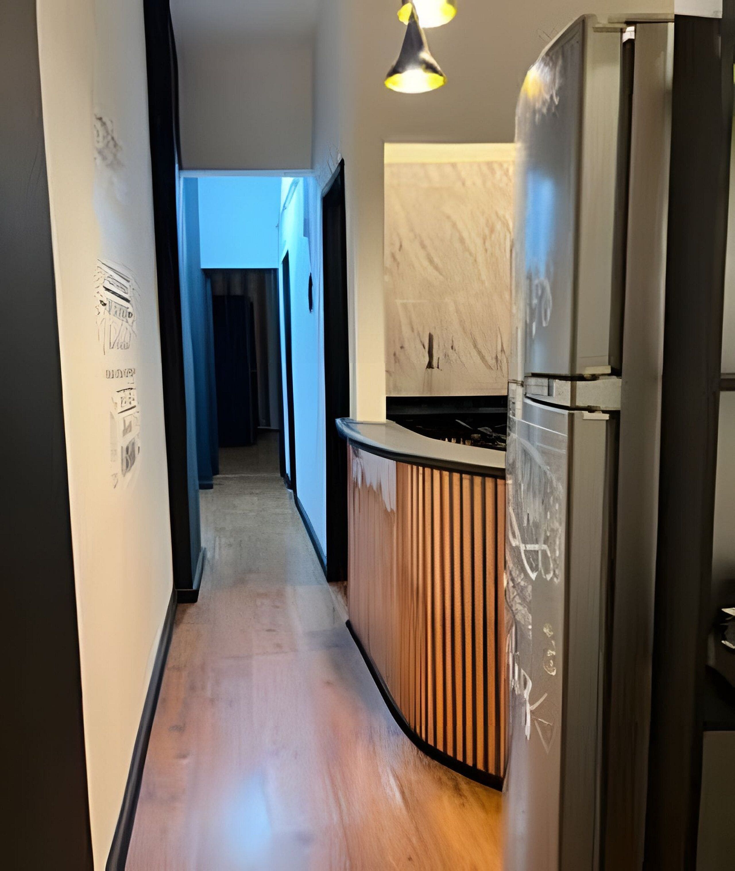 A narrow hallway with a kitchen area on the right, featuring a refrigerator and a stove.