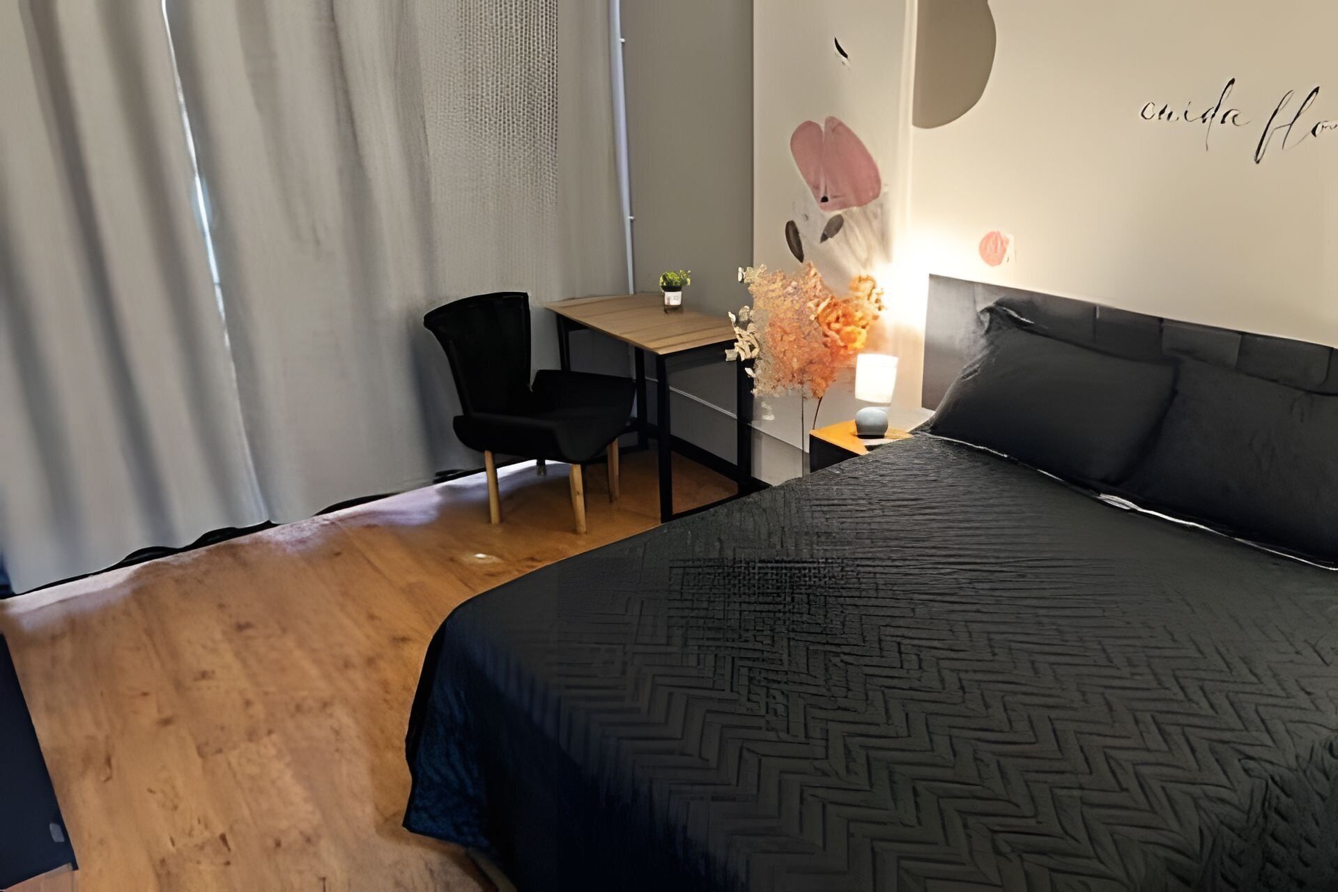 A hotel room with a bed, a desk, a chair, and a wall with a decorative element.