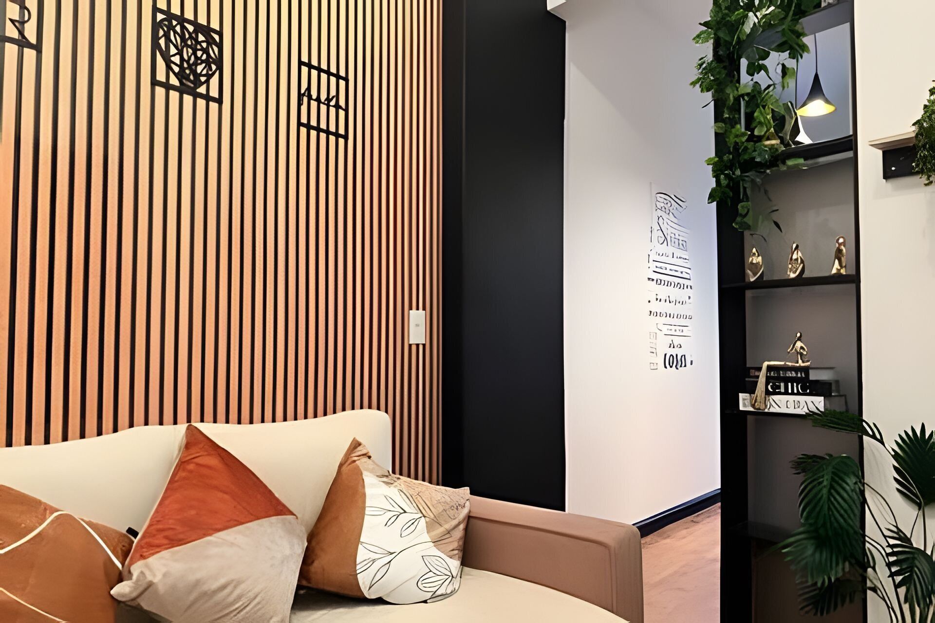 Un interior moderno con un panel de madera, un sofá con cojines, una pared con texto decorativo y una estantería con objetos.