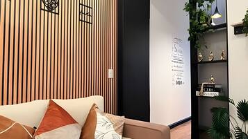 Un interior moderno con un panel de madera, un sofá con cojines, una pared con texto decorativo y una estantería con objetos.