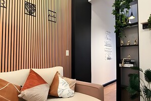 Un interior moderno con un panel de madera, un sofá con cojines, una pared con texto decorativo y una estantería con objetos.