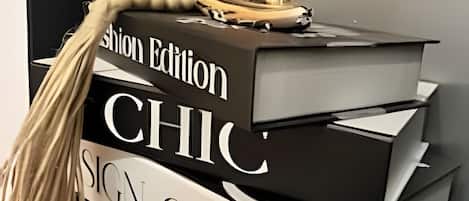 A stack of books with the titles 'Fashion Edition,' 'CHIC,' and 'SIGN CLEAN' on a black shelf.