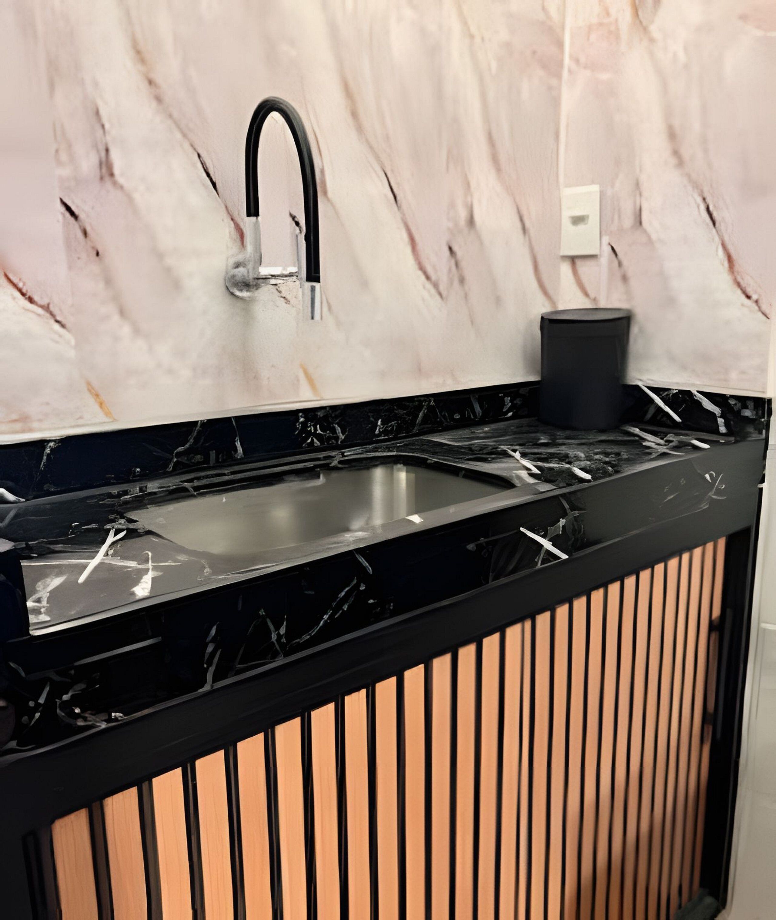 Uma cozinha com bancada preta, pia de aço inoxidável e painel de fundo em mármore.
