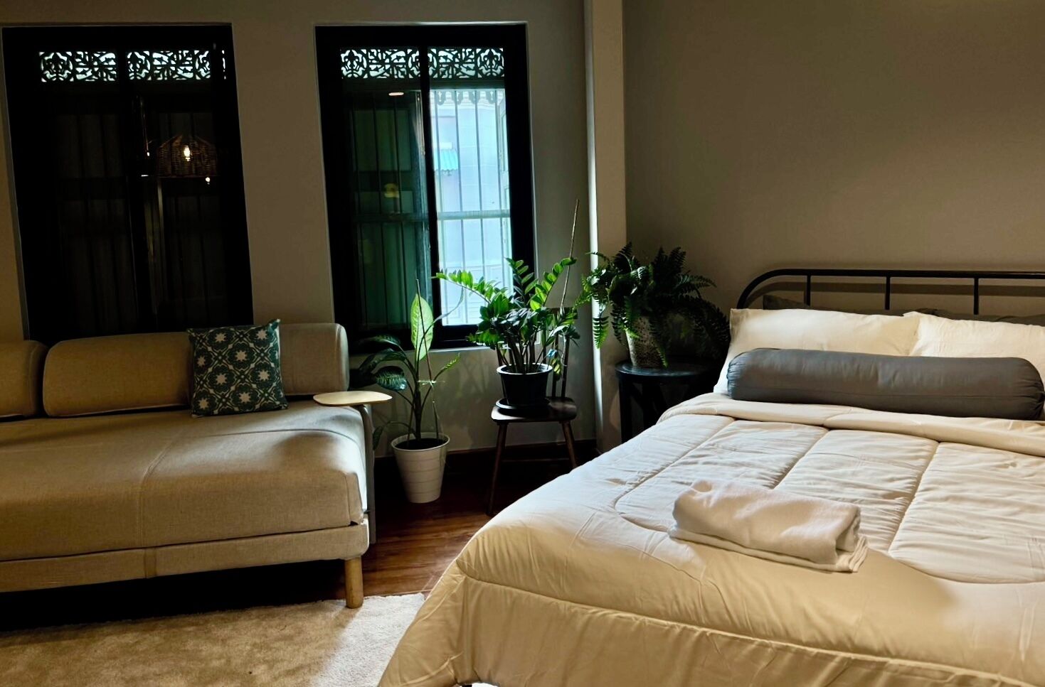 Ein Schlafzimmer mit einem Bett, einem Schlafsofa, einem Nachttisch und zwei Blumentöpfen.