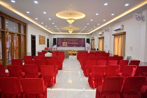 A conference room with rows of red chairs, a stage with a banner, and a chandelier. - BENGALURU VISTA  (Ayodhya)