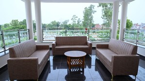 A balcony with two sofas and a small round table, overlooking a green landscape with trees and buildings. - BENGALURU VISTA  (Ayodhya)