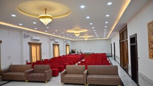 A spacious hall with rows of red chairs, a stage, and a chandelier. - BENGALURU VISTA  (Ayodhya)