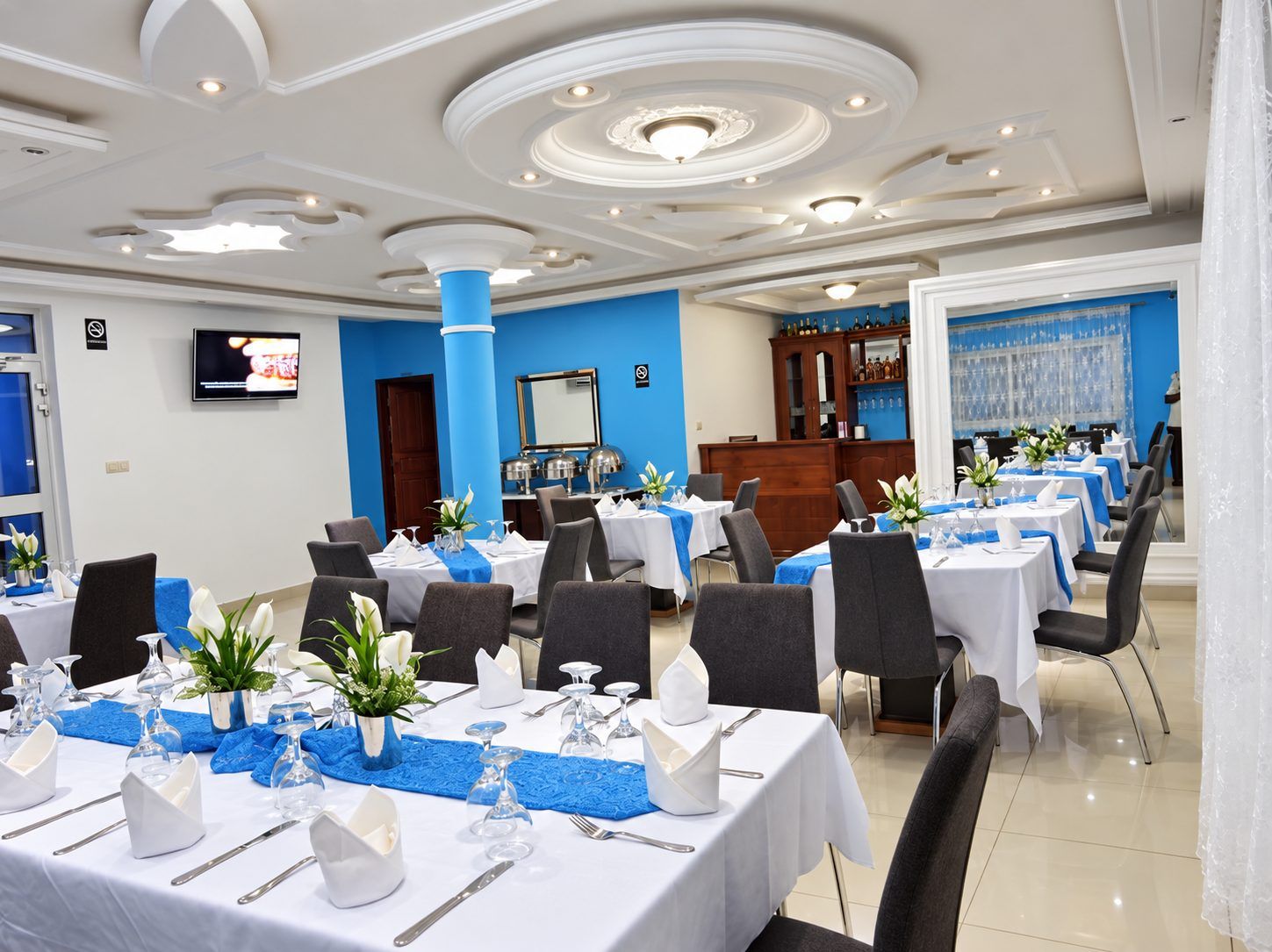 A hotel dining area with tables set for service, a bar area, and a television screen.