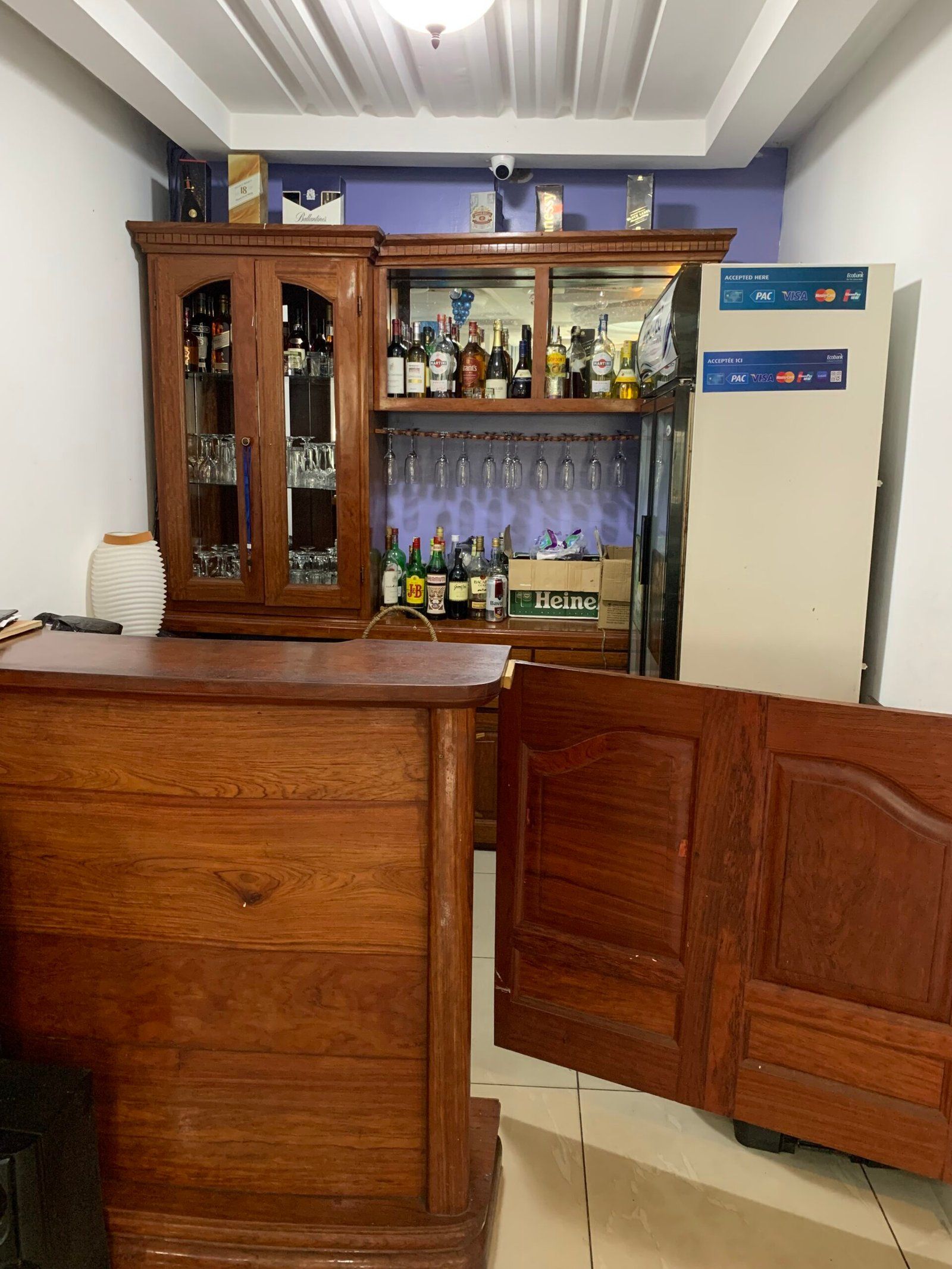 Zona de bar amb un taulell de fusta, un armari per a licors i un frigorífic amb un terminal de pagament.