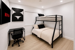 Una cama litera con escritorio y silla, una ventana con persianas, y un televisor de pared mostrando el logotipo de Netflix.