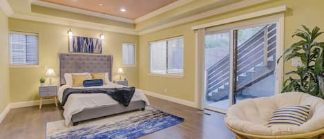 Un dormitorio con cama, mesitas de noche, una silla, un ventanal grande y una escalera.