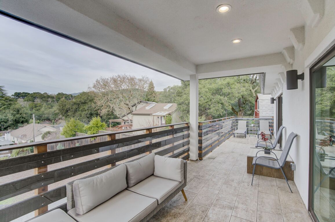 A balcony with a sofa and chairs, a railing, and a view of the surrounding area.