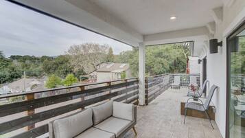 A balcony with a sofa and chairs, a railing, and a view of the surrounding area.