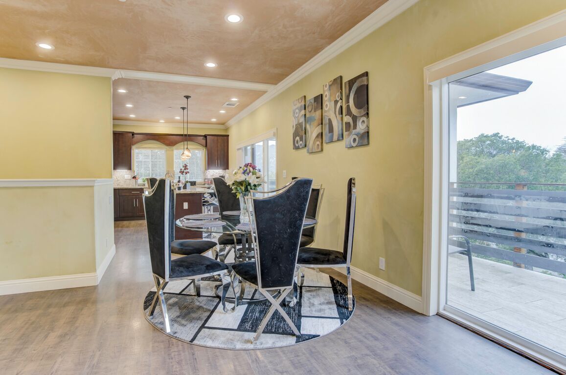 A dining area with a round table and chairs, a kitchen in the background, and a large window with a view.