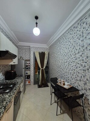 A compact kitchen with a gas stove, a coffee maker, and a dining area with a table and chairs. - Adorable 2-bedroom apartment with AC in welcoming Mohammedia (Mohammedia)
