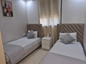 A hotel room with two single beds, a small bedside table with a vase, and a painting on the wall. - Adorable 2-bedroom apartment with AC in welcoming Mohammedia (Mohammedia)