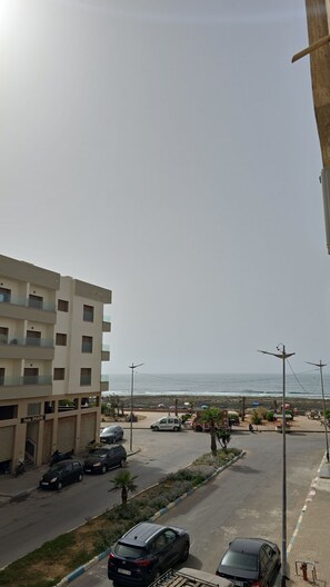 A multi-story building with a parking area, a street with parked cars, and a view of the sea. - Adorable 2-bedroom apartment with AC in welcoming Mohammedia (Mohammedia)