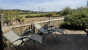 Eine Terrasse mit zwei gestreiften Liegestühlen und einem Holzzaun.