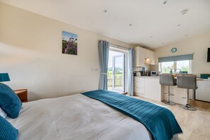 A bedroom with a bed, a view of the kitchen, and a dining area with chairs. - Ashclose Lodge Annexe -  Sherborne, Dorset (Sherborne)