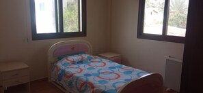 A small, simple bedroom with a bed, bedside table, and a radiator. - 3-bedroom apartment in peaceful Oroklini with cool AC.family friendly (Oroklini)