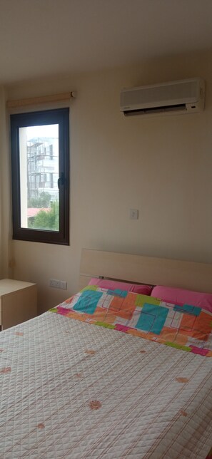 Un dormitorio con cama, ventana, aire acondicionado de pared y puerta.