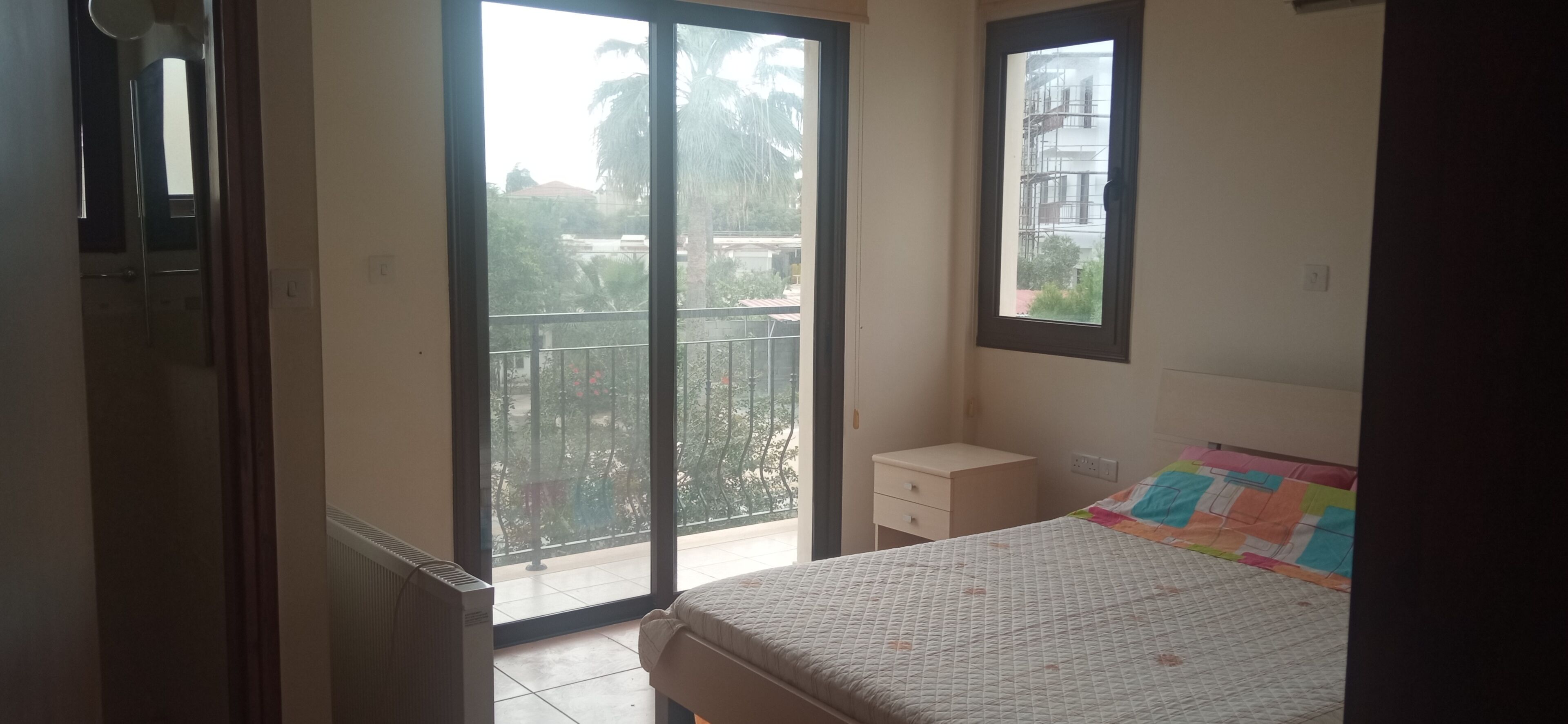 Ein Schlafzimmer mit einem Bett, einem Nachttisch, einem Fenster und Blick ins Freie.