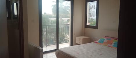 A bedroom with a bed, a nightstand, a window, and a view of the outside.
