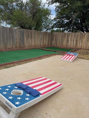 Two GoSports bean bag chairs with American flag designs, set on a concrete patio with a wooden fence and green artificial turf in the background. - Golf Suites by Reserved Rentals (Lubbock)