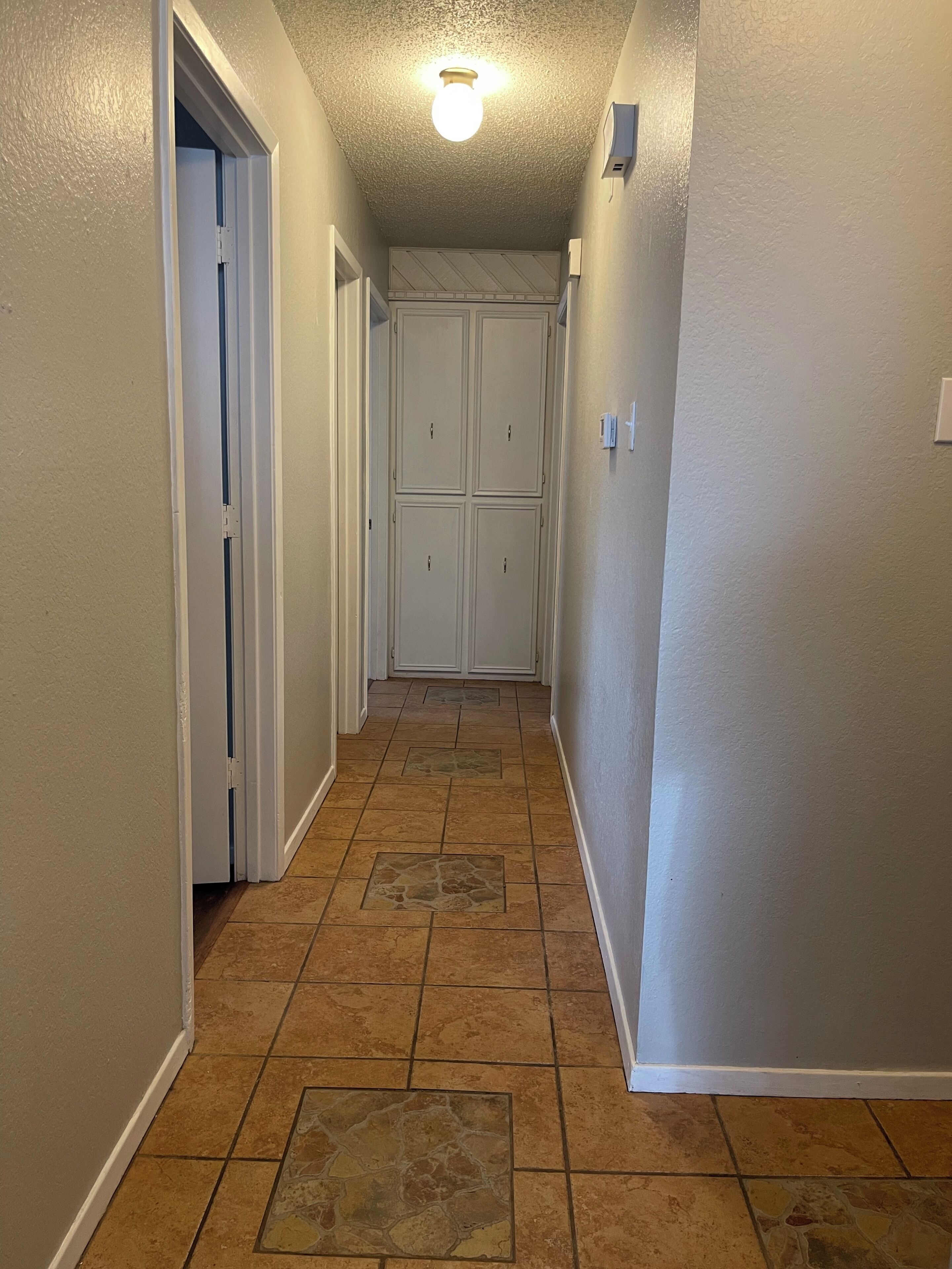 A narrow hallway with a tiled floor, white walls, and a ceiling light fixture.