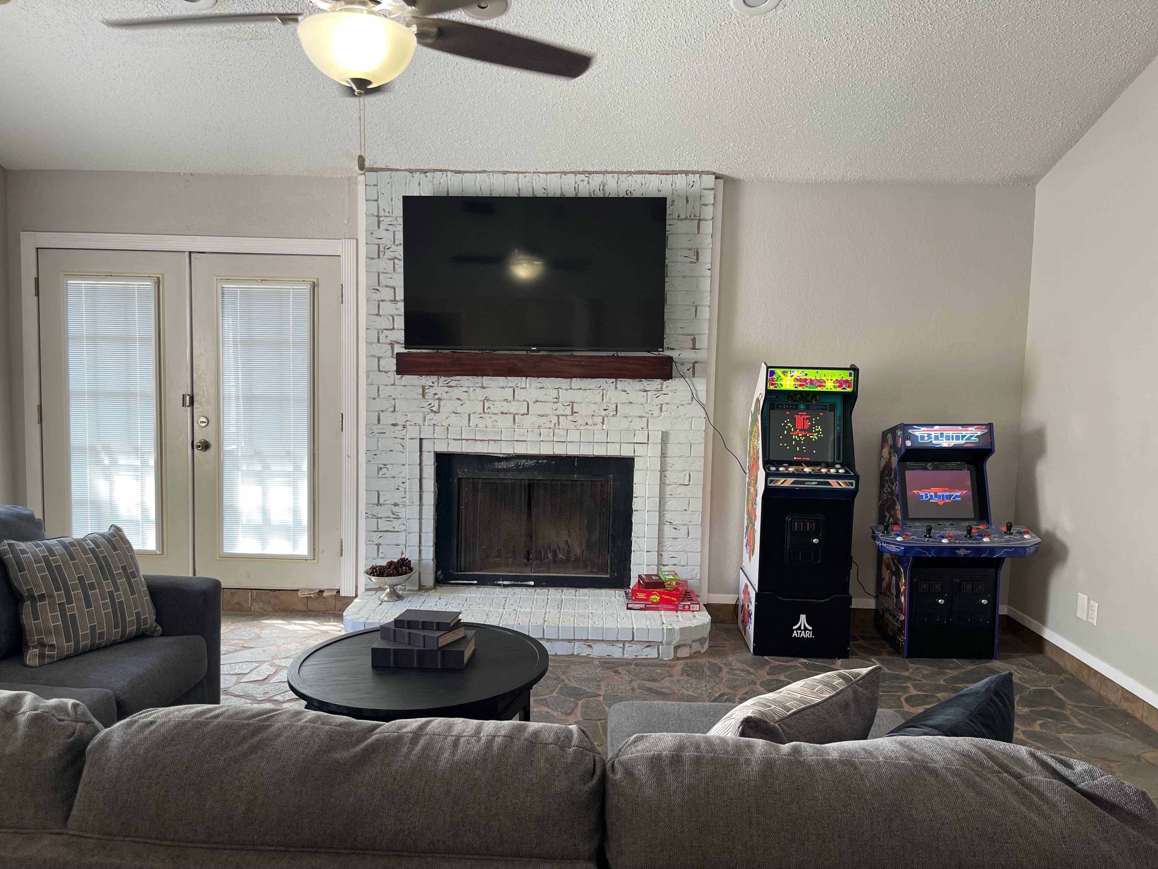 Un salon avec une cheminée, un ventilateur de plafond et une borne d’arcade.