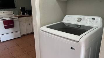 A laundry room with a front-loading washing machine, a stove, and cabinets.
