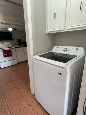 A laundry room with a front-loading washing machine, a stove, and cabinets. - Golf Suites by Reserved Rentals (Lubbock)