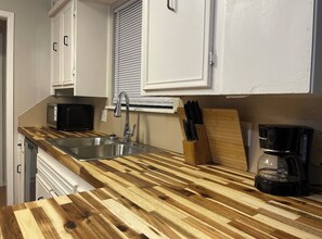A kitchen with a wooden countertop, a sink, a microwave, a coffee maker, and cabinets. - Golf Suites by Reserved Rentals (Lubbock)