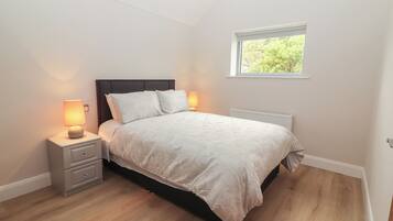 Un dormitorio con cama, mesitas de noche, ventana y radiador.