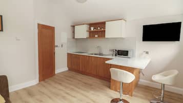 A modern kitchen with wooden cabinets, a white countertop, a built-in microwave, and a bar stool.