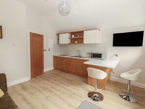 A modern kitchen with wooden cabinets, a white countertop, a built-in microwave, and a bar stool.