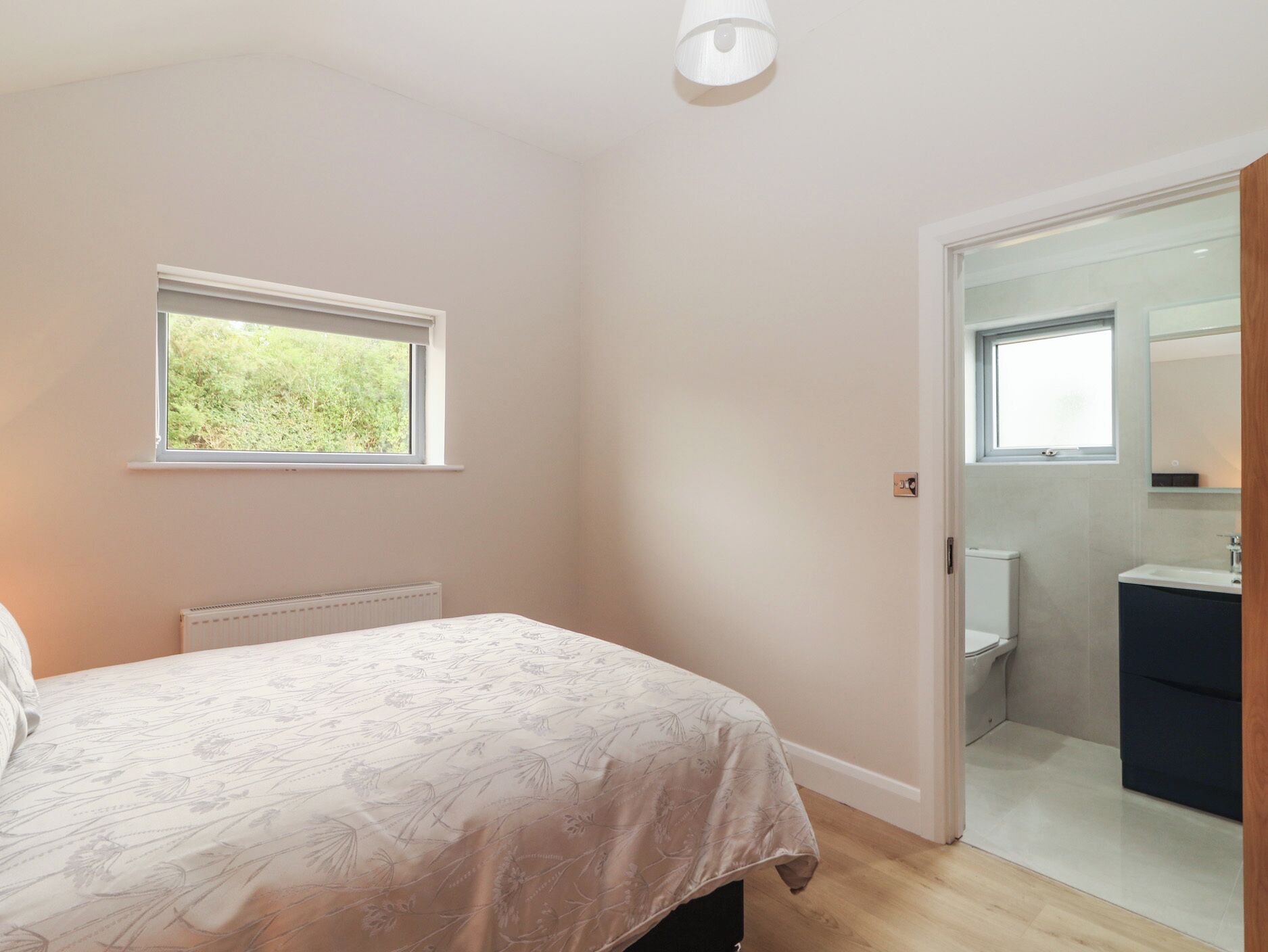 Un dormitorio con cama, ventana, radiador y un baño visible a través de una puerta abierta.