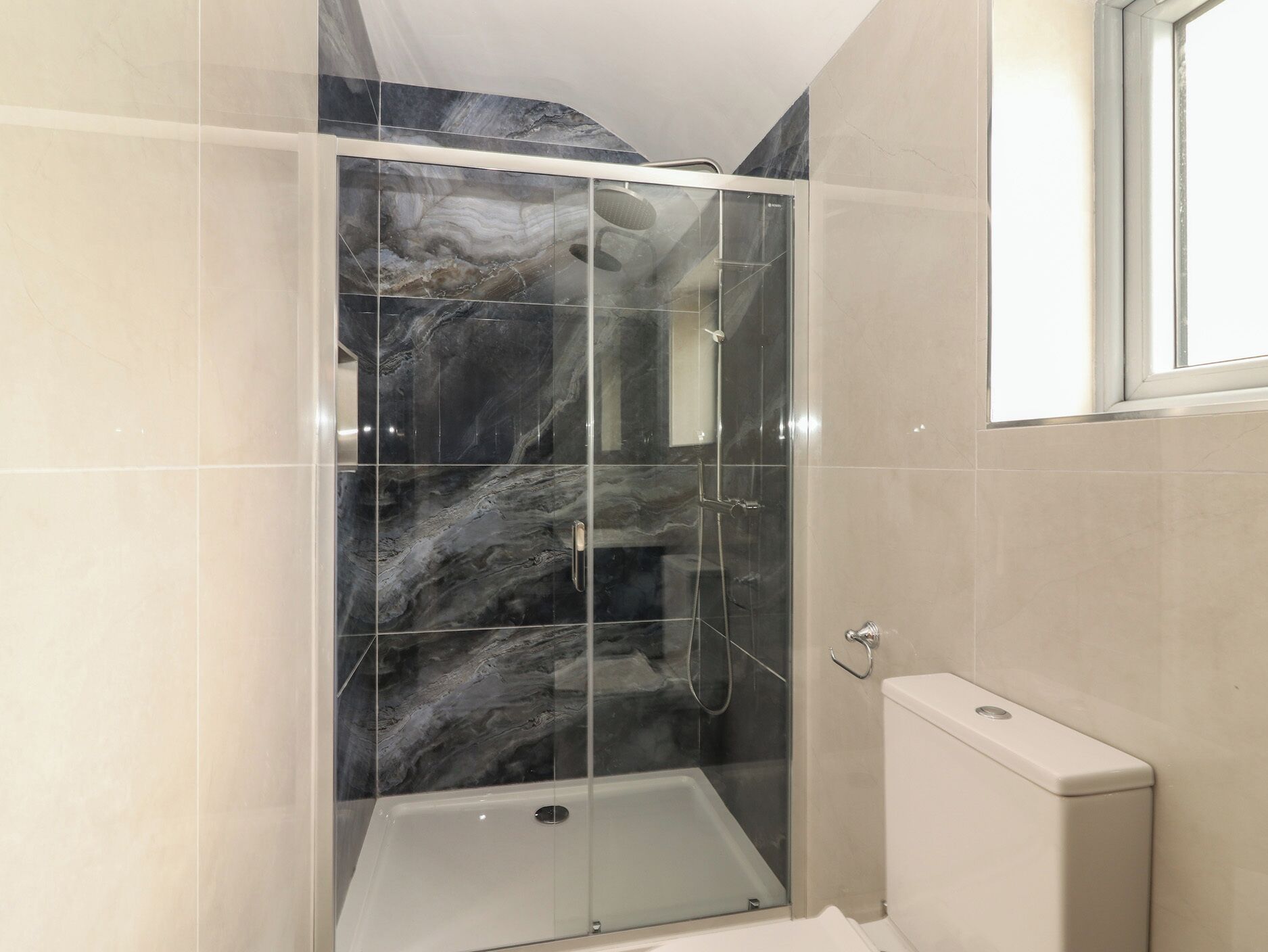 A shower enclosure with a glass door, a white bathtub, and a toilet.