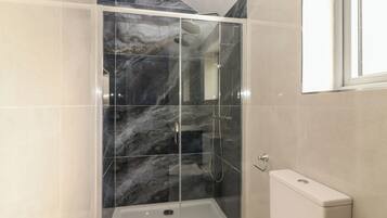 A shower enclosure with a glass door, a white bathtub, and a toilet.