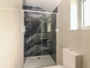 A shower enclosure with a glass door, a white bathtub, and a toilet.