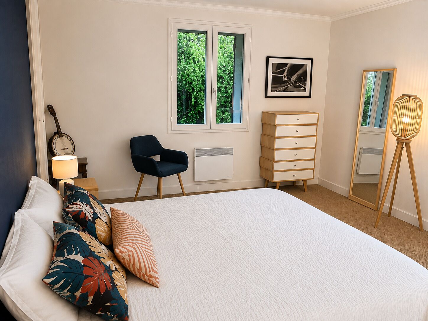 Una camera da letto con un letto, una sedia, una cassettiera, una lampada, una chitarra e una finestra vista sul verde.