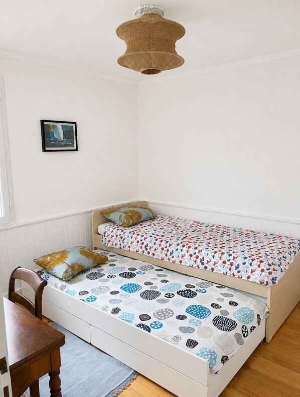 A bedroom with a bunk bed, a wooden chair, a framed picture on the wall, and a hanging light fixture.