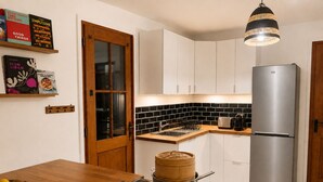 A modern kitchen with a built-in stove, a stainless steel refrigerator, and a wooden dining table. - House in Yvoire between Lake and Village (Yvoire)