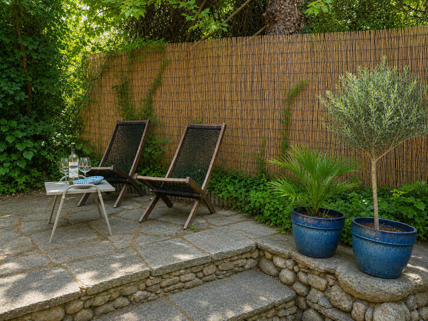 Une terrasse avec deux chaises en bois, une table avec des verres à vin et des plantes en pot.