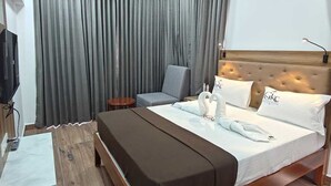 Camera d'albergo con un letto, una testiera, una televisione, una scrivania e una finestra con tende.
