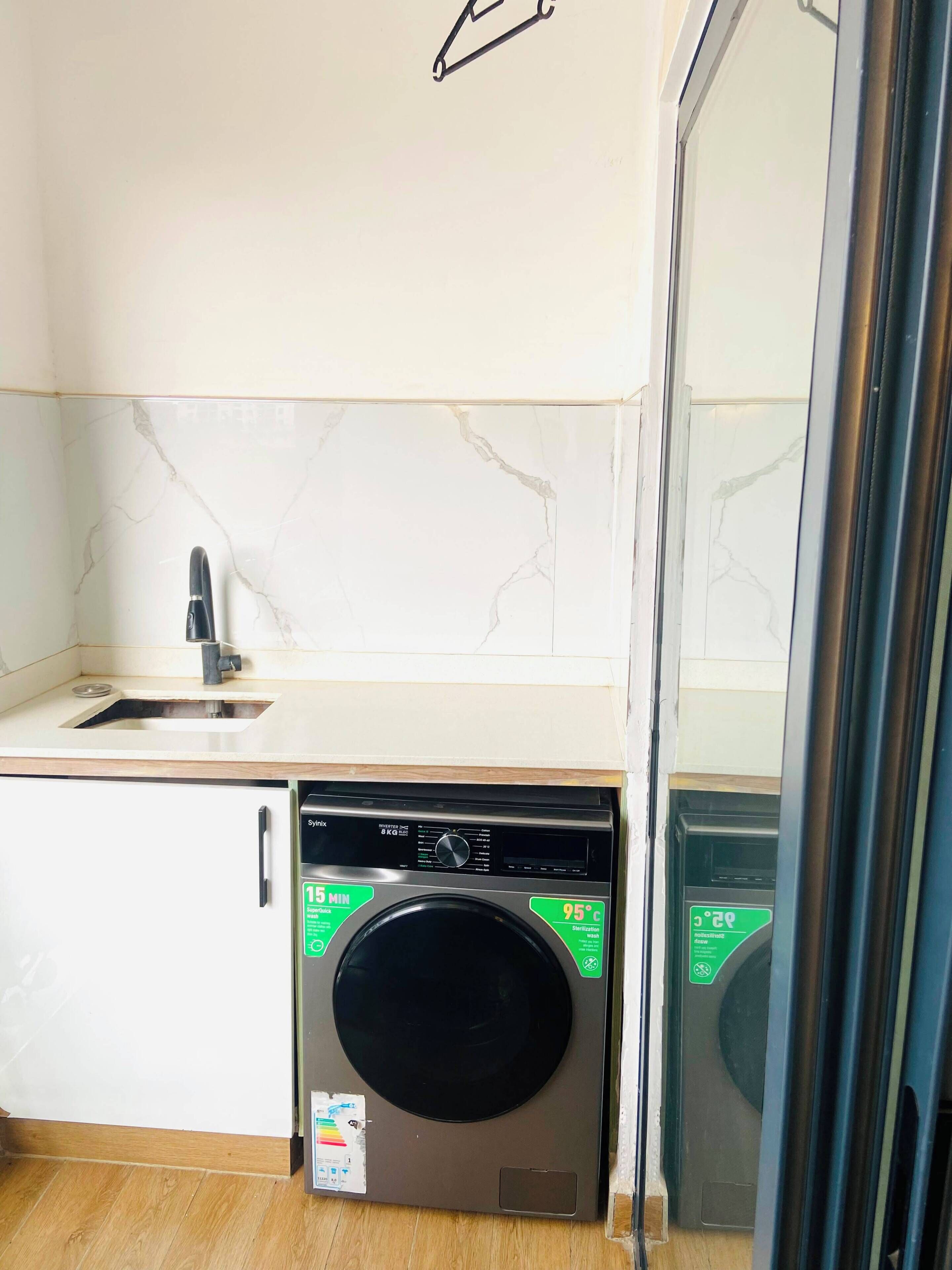 A compact kitchen with a built-in washing machine, a sink, and a mirror.